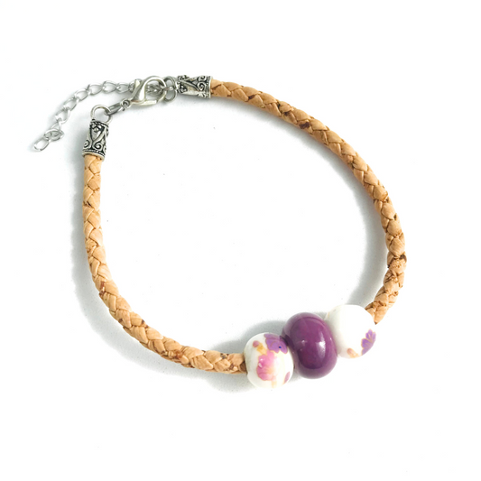 Pulsera de Corcho Trenzado Portugués Dije al centro de Color Morado Ciruela y 2 dijes a los lados blancos con flores rosadas y moradas. Detalles metálicos de zamac aleación de metales hipoalergénicos cadena para ajustar tamaño